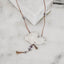 Silver butterfly pendant with engraved wings and raw amethyst drops hanging from the body, on a brown tassel cord with gemstone accents displayed on a marble surface.