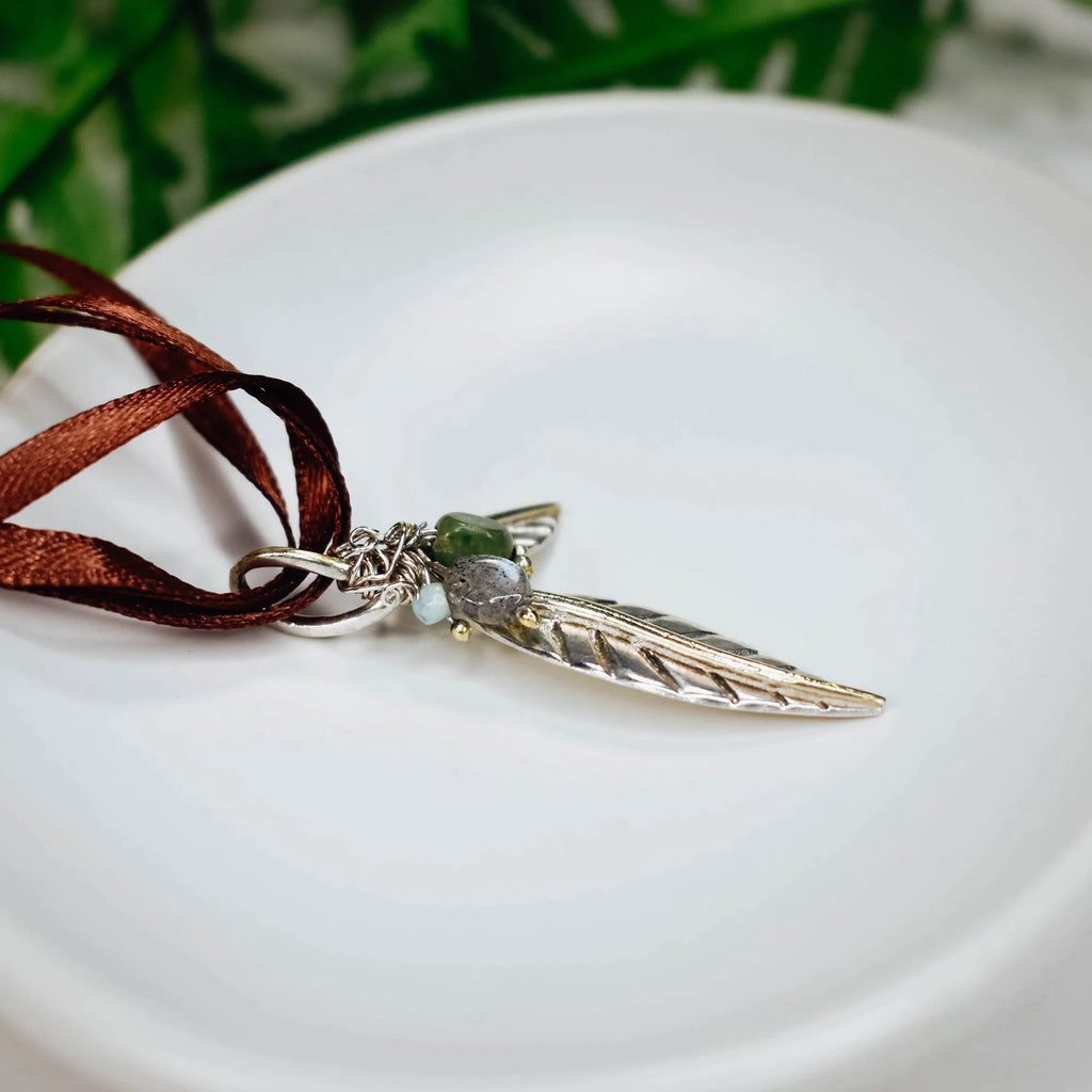 Side angle view of a silver leaf pendant showing the detailed veined leaf forms and wire-wrapped gemstone cluster with moonstone, turquoise and green stone on a brown satin ribbon cord.