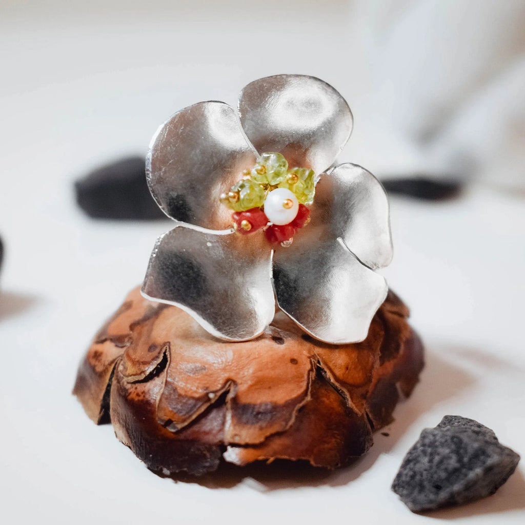 Close-up of a large silver flower ring showing the four sculpted brushed petals and the colourful gemstone centre cluster with green crystal, red coral, pearl and gold bead details.