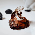 Side view of a silver flower ring showing the plain polished adjustable silver band and the underside of the sculpted flower head on a pine cone display.
