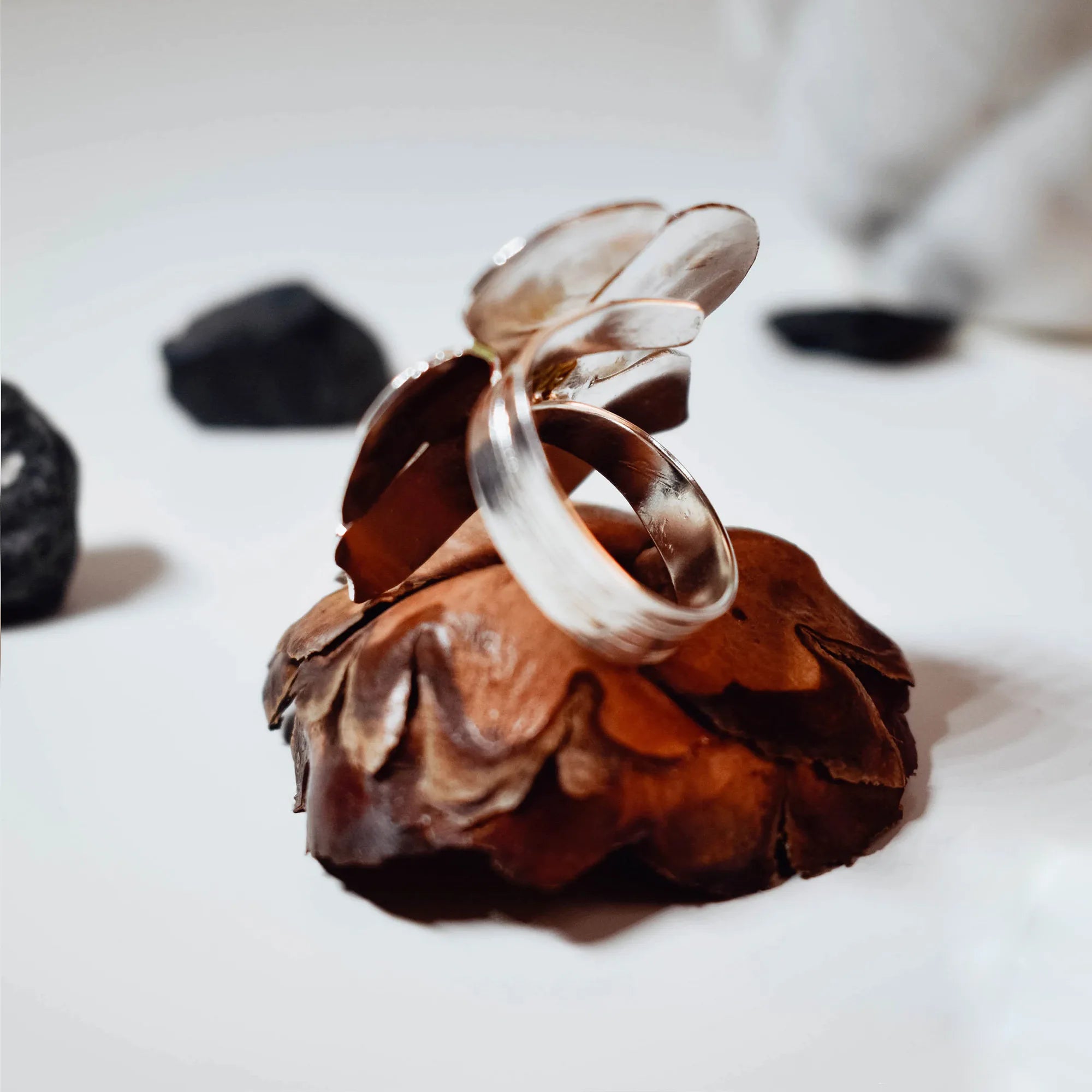 Side view of a silver flower ring showing the plain polished adjustable silver band and the underside of the sculpted flower head on a pine cone display.