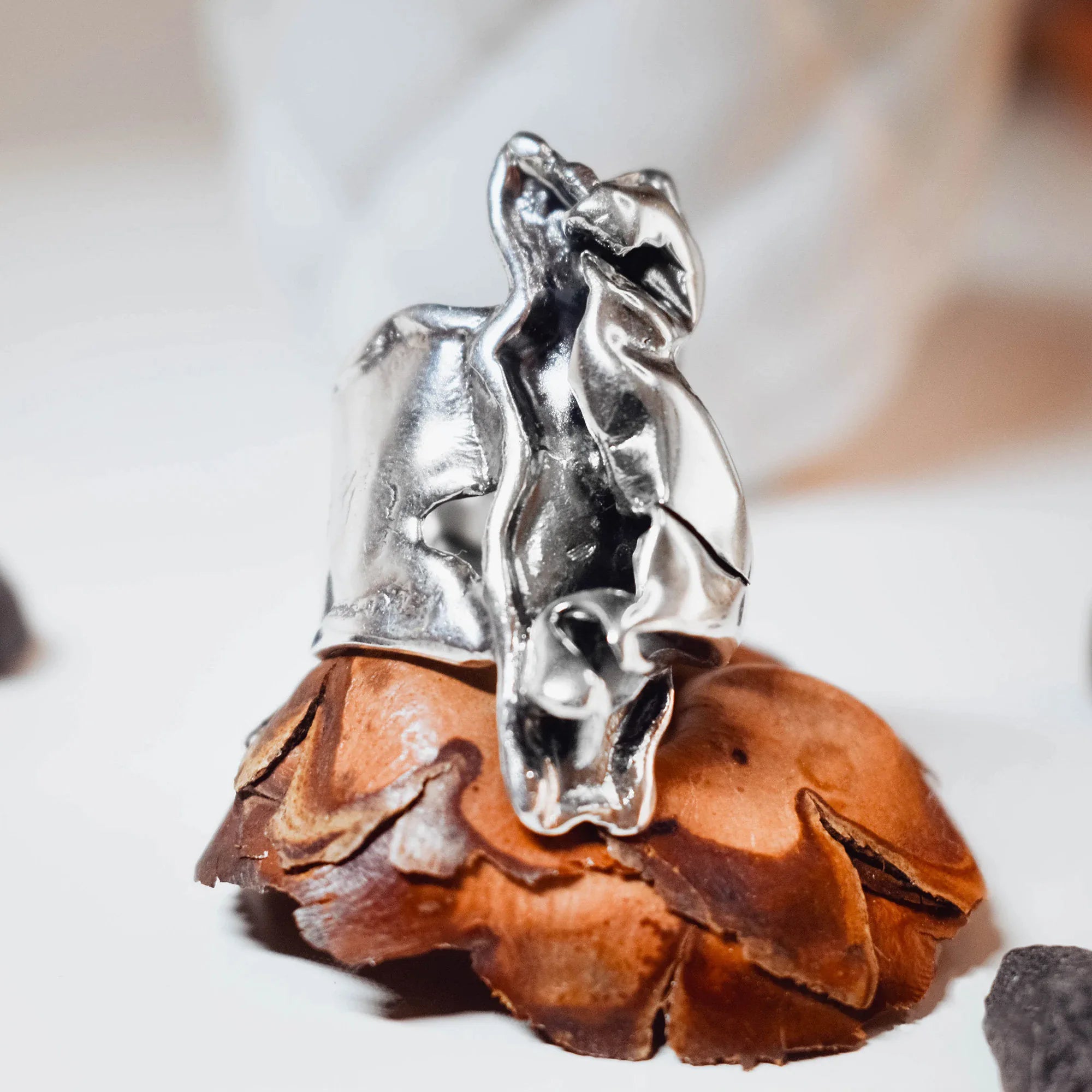 Side view of a large sculptural silver ring showing the folded and crumpled polished silver surface with multiple facets and planes on a pine cone display.