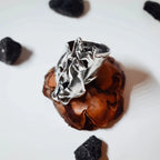 Top-down view of a large sculptural silver ring showing the full expanse of the crumpled polished silver surface and adjustable band on a pine cone display.