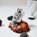  Large sculptural silver ring with a dramatic crumpled free-form polished surface displayed on a pine cone with black stones around it, side view.