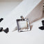 Square hammered silver pendant with softly rounded corners and a smooth fildisi cabochon centre stone, displayed against a white surface with black stones around it.