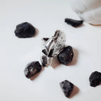 Front view of a sculptural silver ring showing the full crumpled polished silver surface surrounded by black rocks on a white surface.