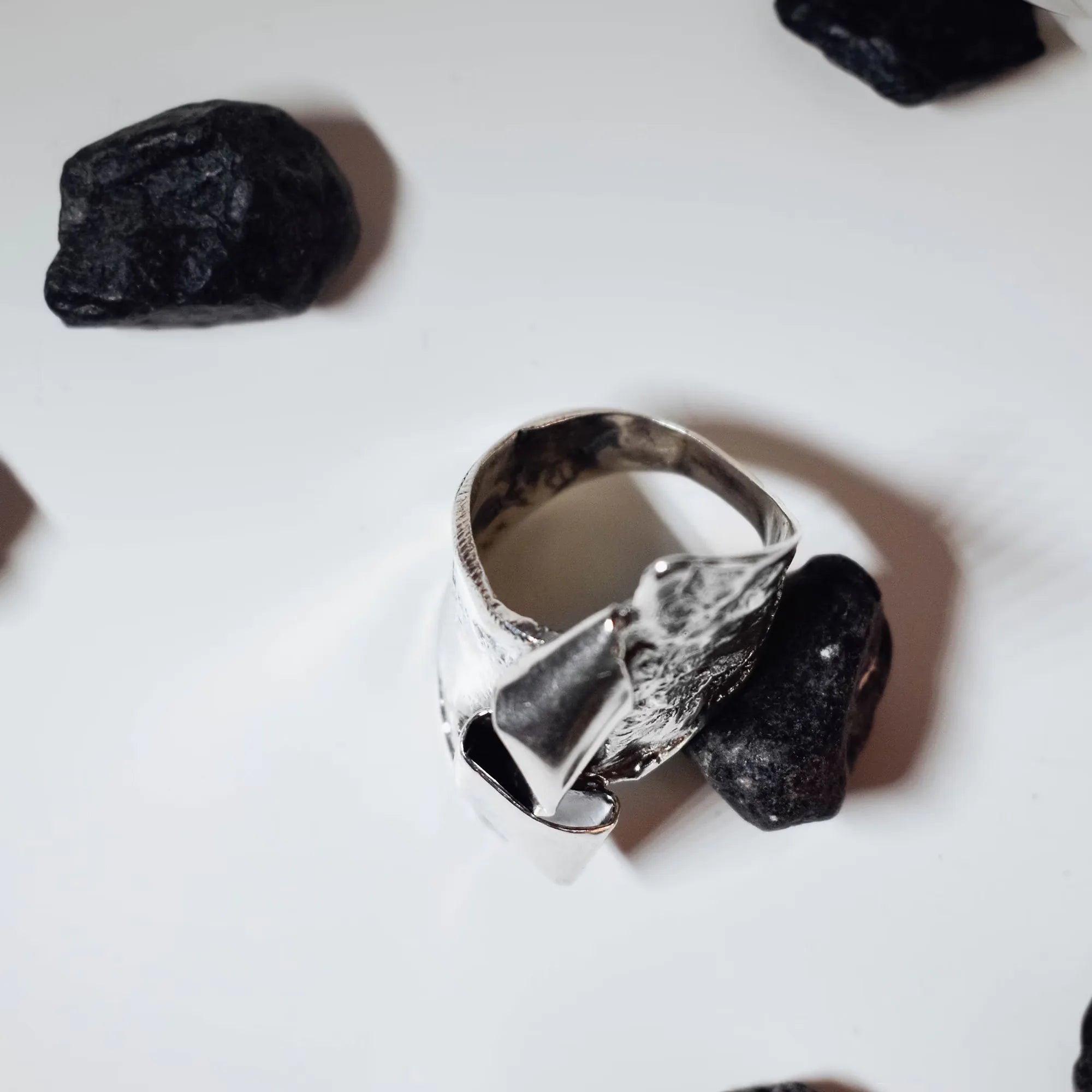 Top-down view of a sculptural silver ring showing the adjustable band and the underside of the crumpled silver sculptural top on a white surface.