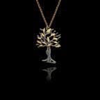 Perspective view of an oxidised silver olive tree pendant with gold leaves on a chain against a black background