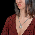 Woman wearing a necklace with an oval pendant, set against a black background