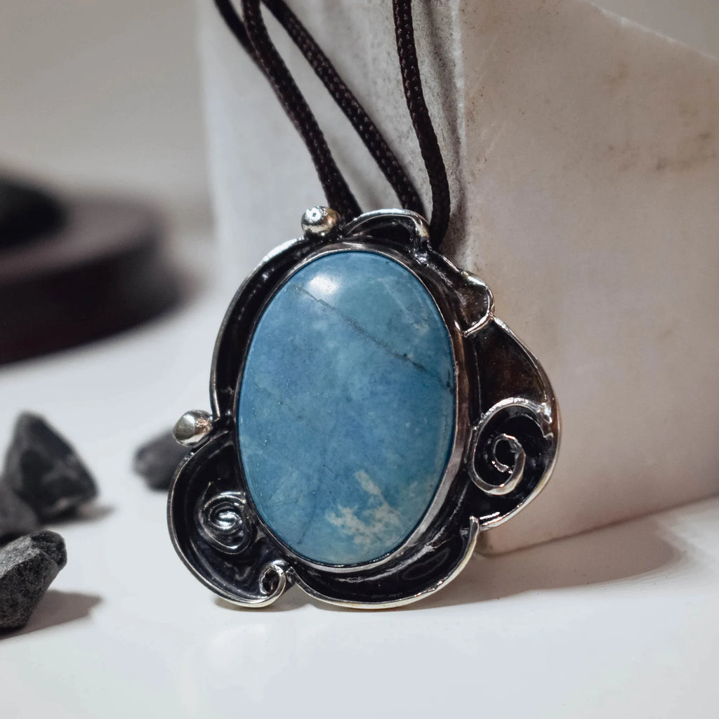 Front view of a large oval chaolite pendant showing the natural blue veining of the stone and the decorative oxidised silver scroll frame with ball accents on a dark cord.