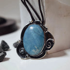 Front view of a large oval chaolite pendant showing the natural blue veining of the stone and the decorative oxidised silver scroll frame with ball accents on a dark cord.