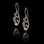 Angled side view of a pair of silver earrings with gold fish design on a black background