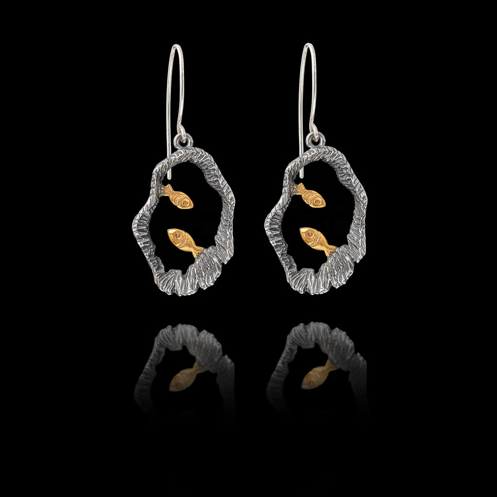 Pair of silver earrings with gold fish design on a black background