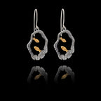 Pair of silver earrings with gold fish design on a black background