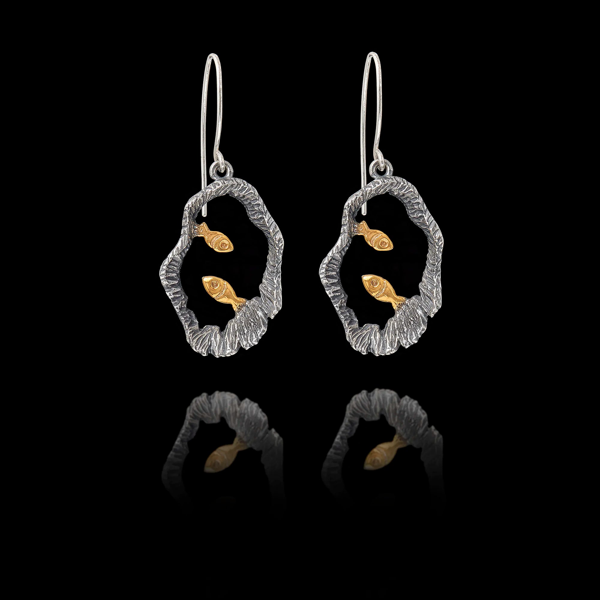 Pair of silver earrings with gold fish design on a black background