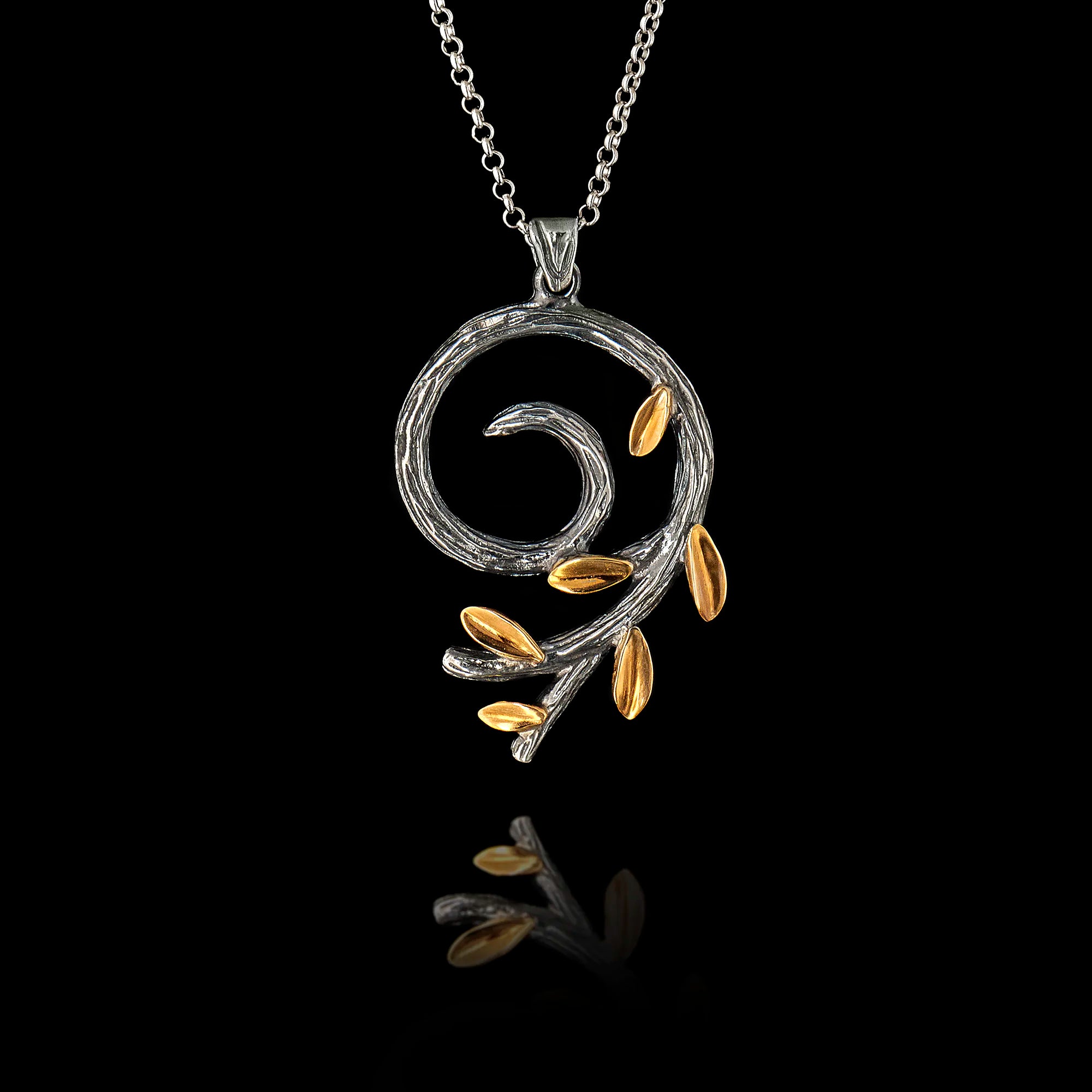 a silver spiral olive branch pendant on a chain, featuring an oxidized stem and gold-plated leaves.