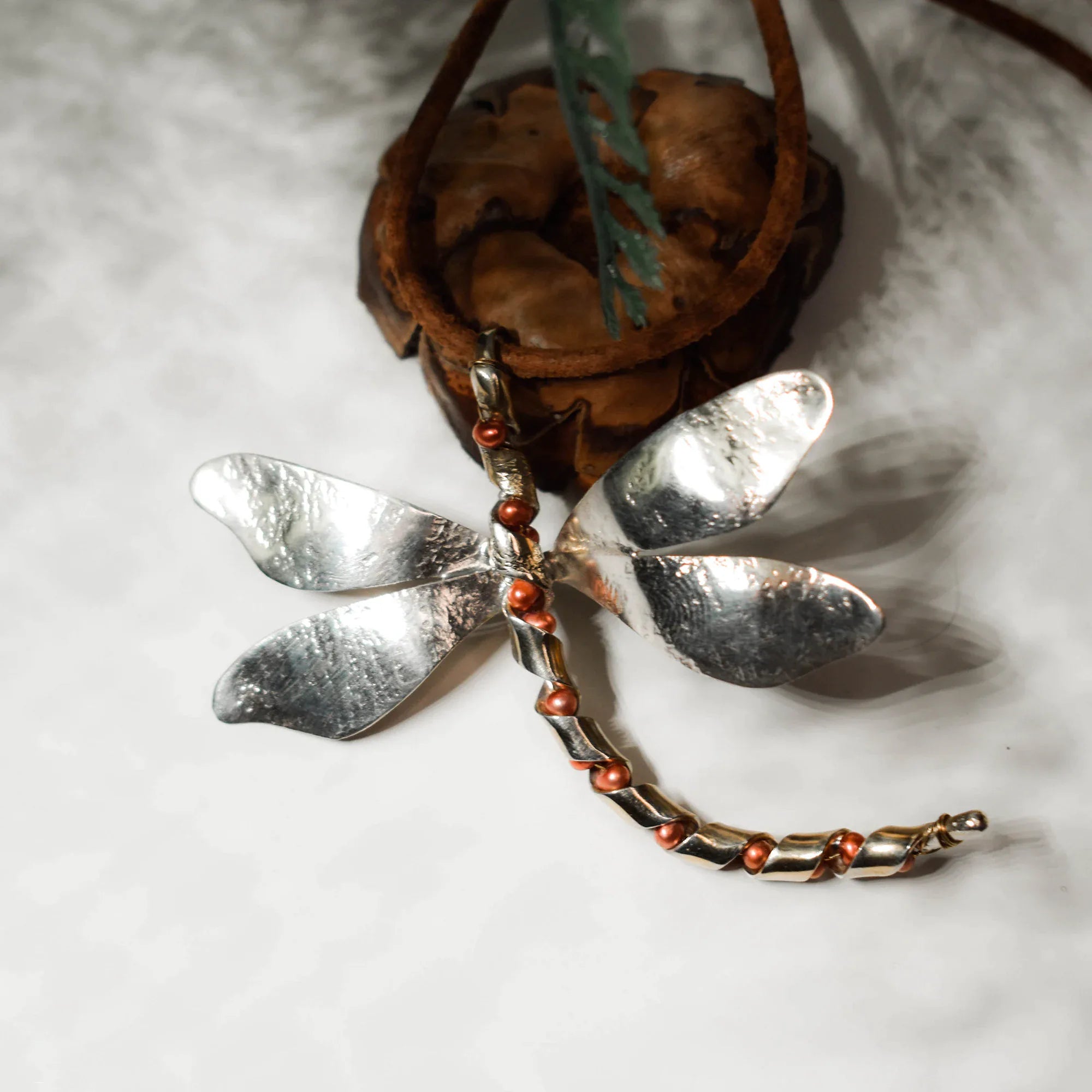 Large silver dragonfly pendant with four broad hammered wings and a segmented silver body with copper-toned freshwater pearl accents, displayed on a white surface with a leather cord. Main image