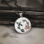 Round pendant with koi fish design on a wooden surface