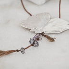 Close-up of a silver butterfly pendant showing the raw amethyst and purple gemstone chip drops hanging from the body with tassel cord ends and small knotted gemstone accents.