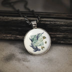 silver pendant featuring blue koi fish swimming in stylized water with golden ginkgo leaves on a wooden background
