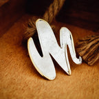 Close-up of an abstract wave silver pendant showing the raw pitted texture of the silver surface and smooth polished edge detail on a wooden surface.