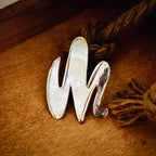 Abstract wave silver pendant with raw textured centre and polished silver edges in a flowing three-crest form, displayed on a wooden surface with a jute rope.