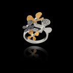 Angled top view of an adjustable 925 sterling silver ring featuring a cluster of four flowers in silver, gold, and oxidized finishes.