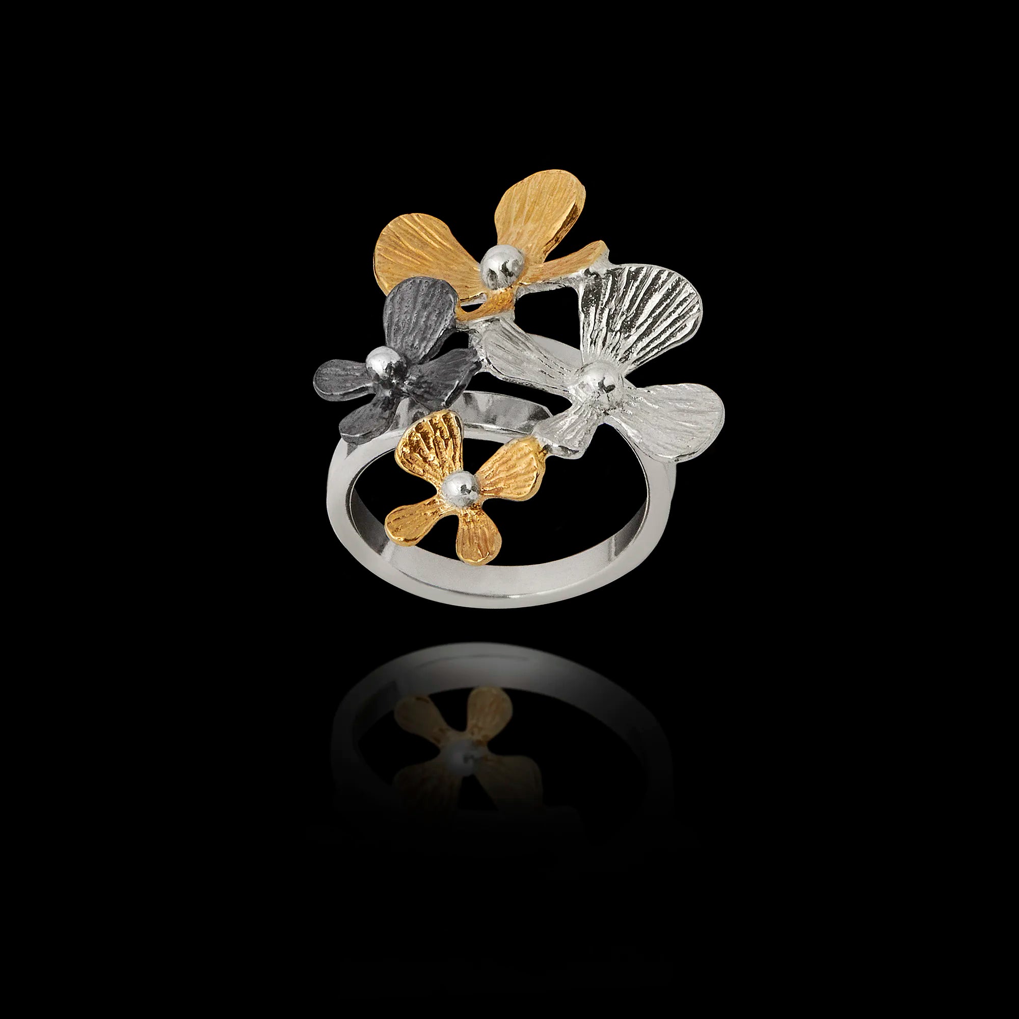 Angled top view of an adjustable 925 sterling silver ring featuring a cluster of four flowers in silver, gold, and oxidized finishes. Main image