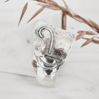 Close-up of an abstract face silver pendant showing the contrast between the deeply textured upper surface with raised nose and lip details and the smooth polished silver lower section.