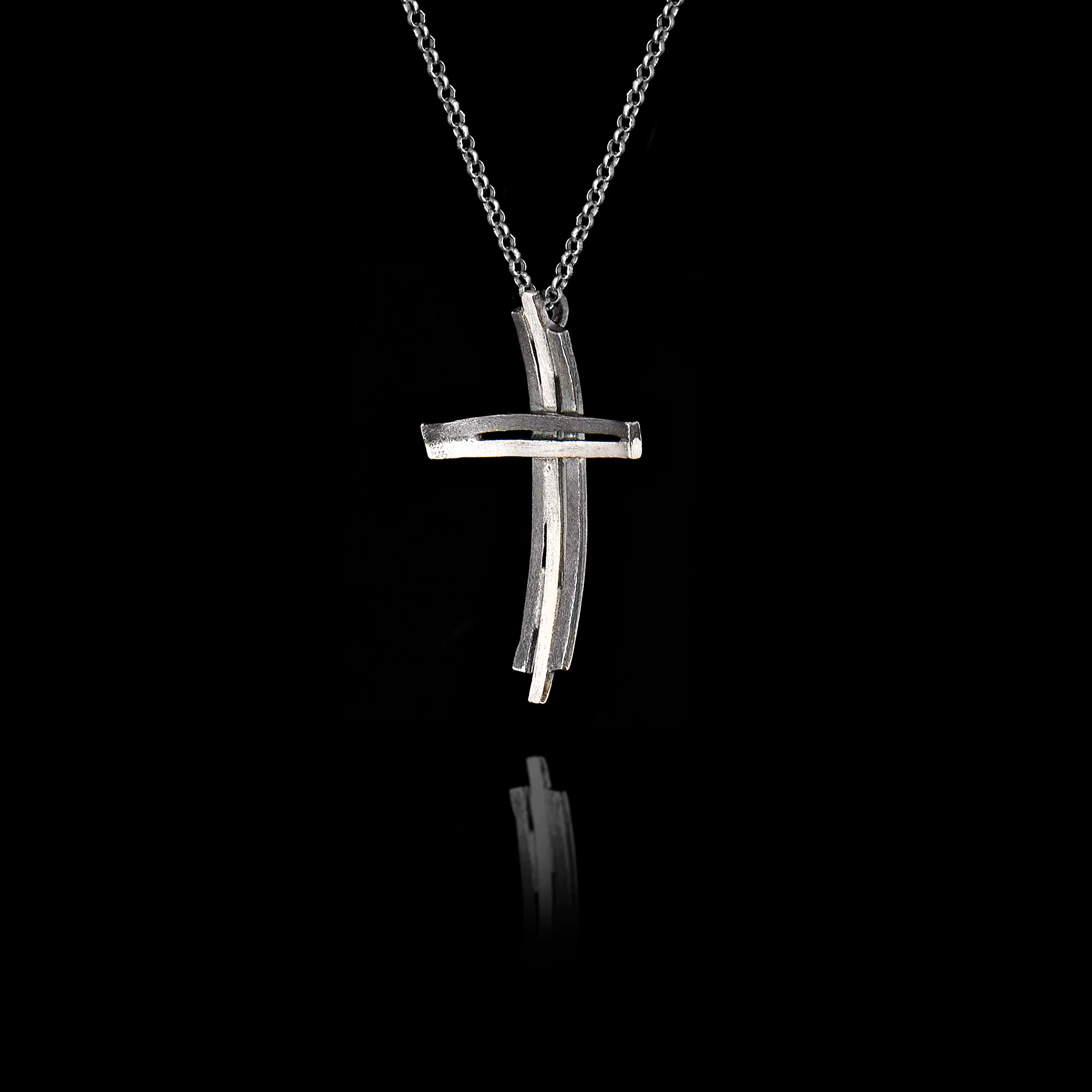 Side angle view of a handcrafted 925 sterling silver modern cross pendant showing the layered parallel bars and curved horizontal element with oxidised and rhodium-plated finish on a silver chain.