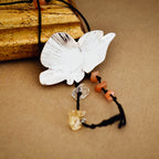 Close-up of a silver butterfly pendant showing the brushed engraved wing detail with orange agate and pale honey crystal chip drops hanging from the body on a black tassel cord.