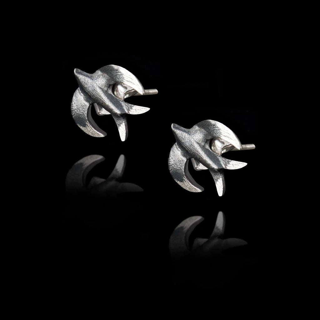 Angled side view of a pair of silver stud earrings shaped like swallows with a dark oxidized finish.