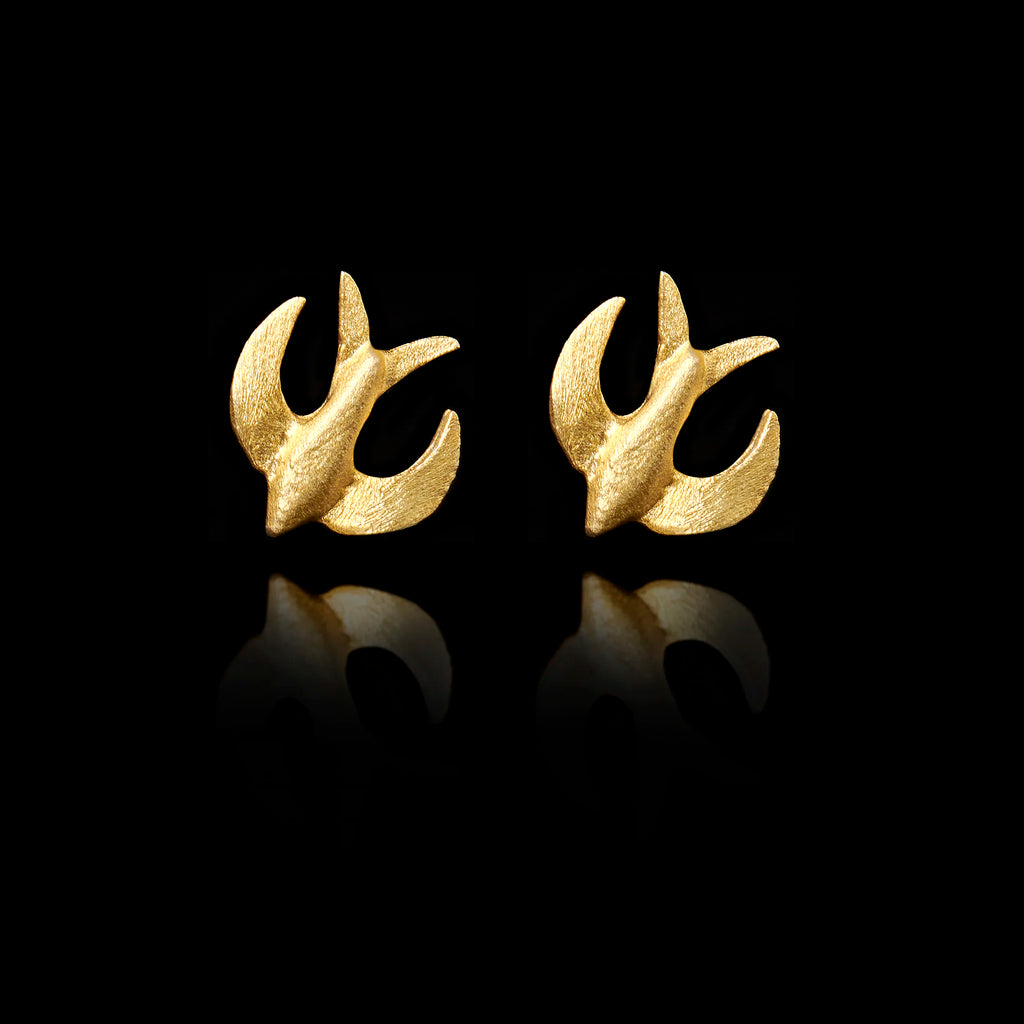 Front view of  gold stud earrings shaped like swallows in flight on black background.