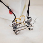Close-up of an oxidised silver bench pendant showing the gold-plated wire heart detail, twisted silver wire sides and horizontal bar bench structure on a double-strand black cord.