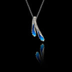 Side angle view of a handcrafted 925 sterling silver blue enamel pendant showing two organic fanned forms with crushed enamel crystal fill on a silver chain against a black background.