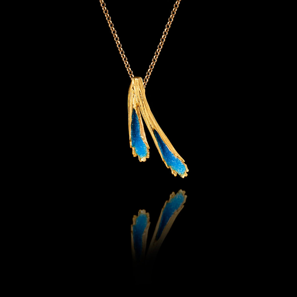 Side angle view of a gold pendant featuring two textured forms filled with vivid blue crushed enamel crystals, hanging on a gold chain against a black background.