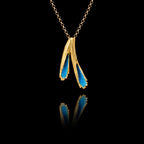 A gold pendant featuring two textured forms filled with vivid blue crushed enamel crystals, hanging on a gold chain against a black background.