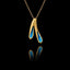 A gold pendant featuring two textured forms filled with vivid blue crushed enamel crystals, hanging on a gold chain against a black background.