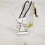 Rectangular silver pendant with bark-textured oxidised surface and raised polished heart, arrow, square, leaf and horizontal bar details on a black cord against a marble surface.