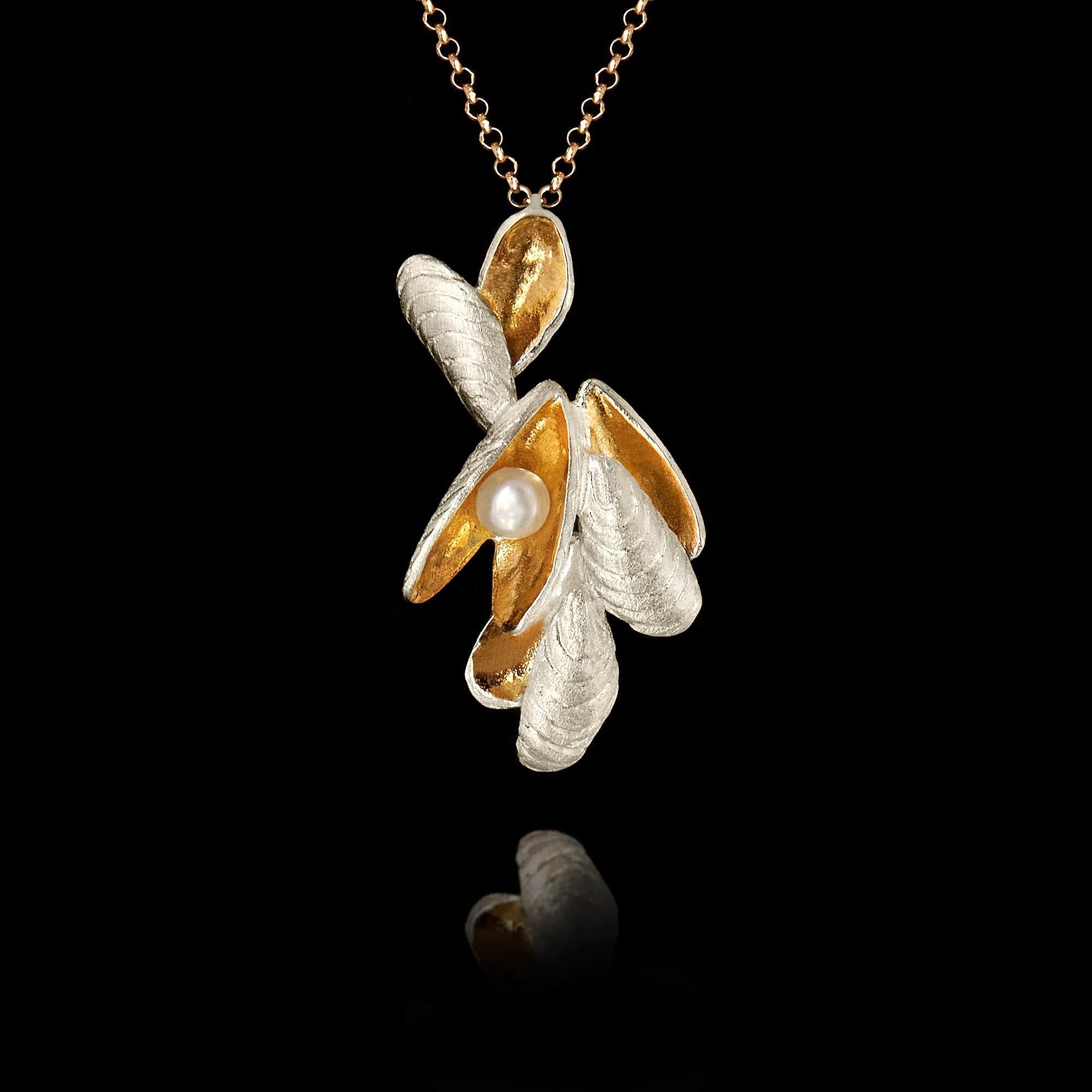 Handcrafted 925 sterling silver shell cluster pendant with rhodium-plated exterior and gold-plated interior shell forms cradling a freshwater pearl, hanging on a gold chain against a black background. Main image