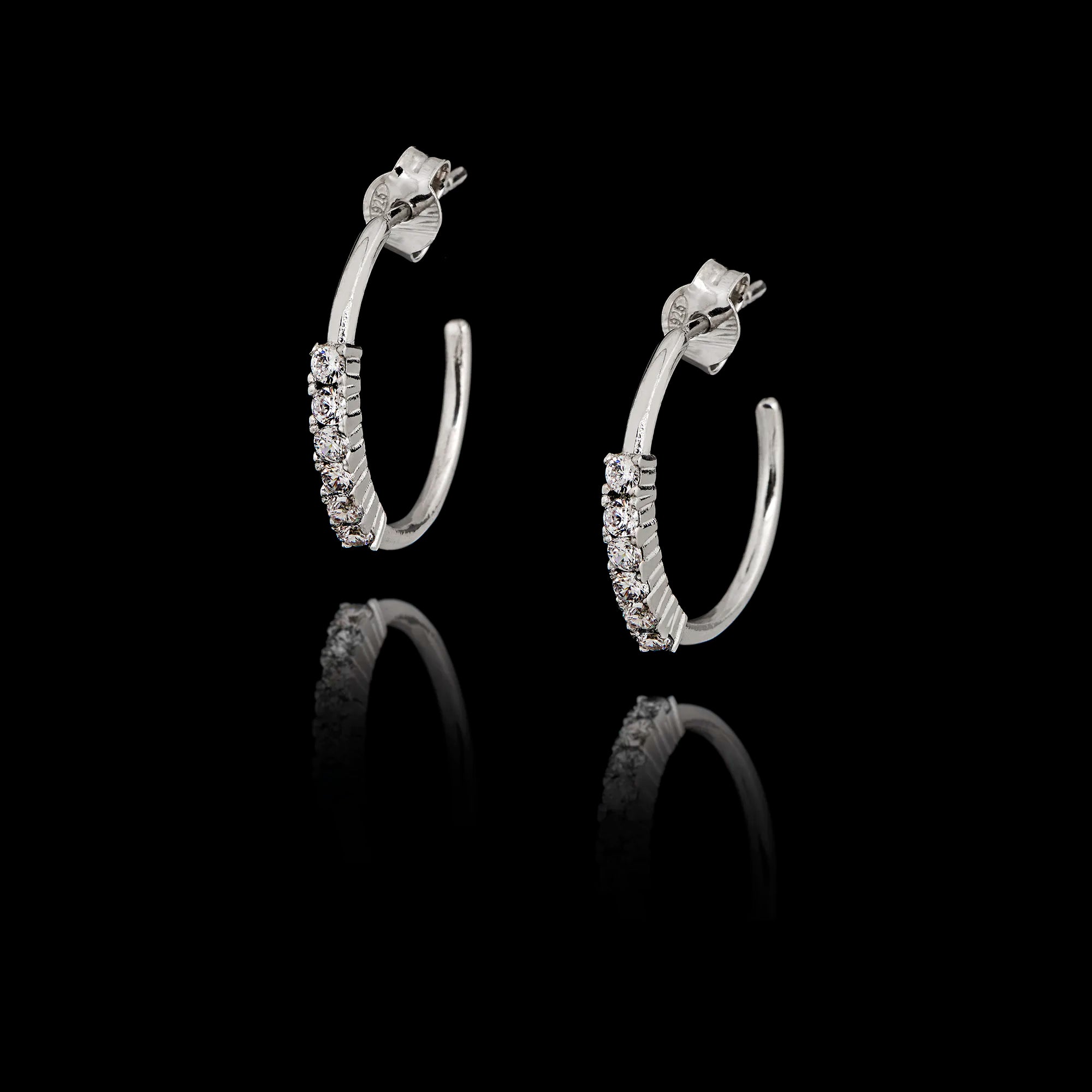 Silver open hoop earrings with clear zircon stones set along the front curve in a black background. Main image