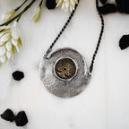Silver pendant necklace with intricate design on a white surface with flowers and black stones.