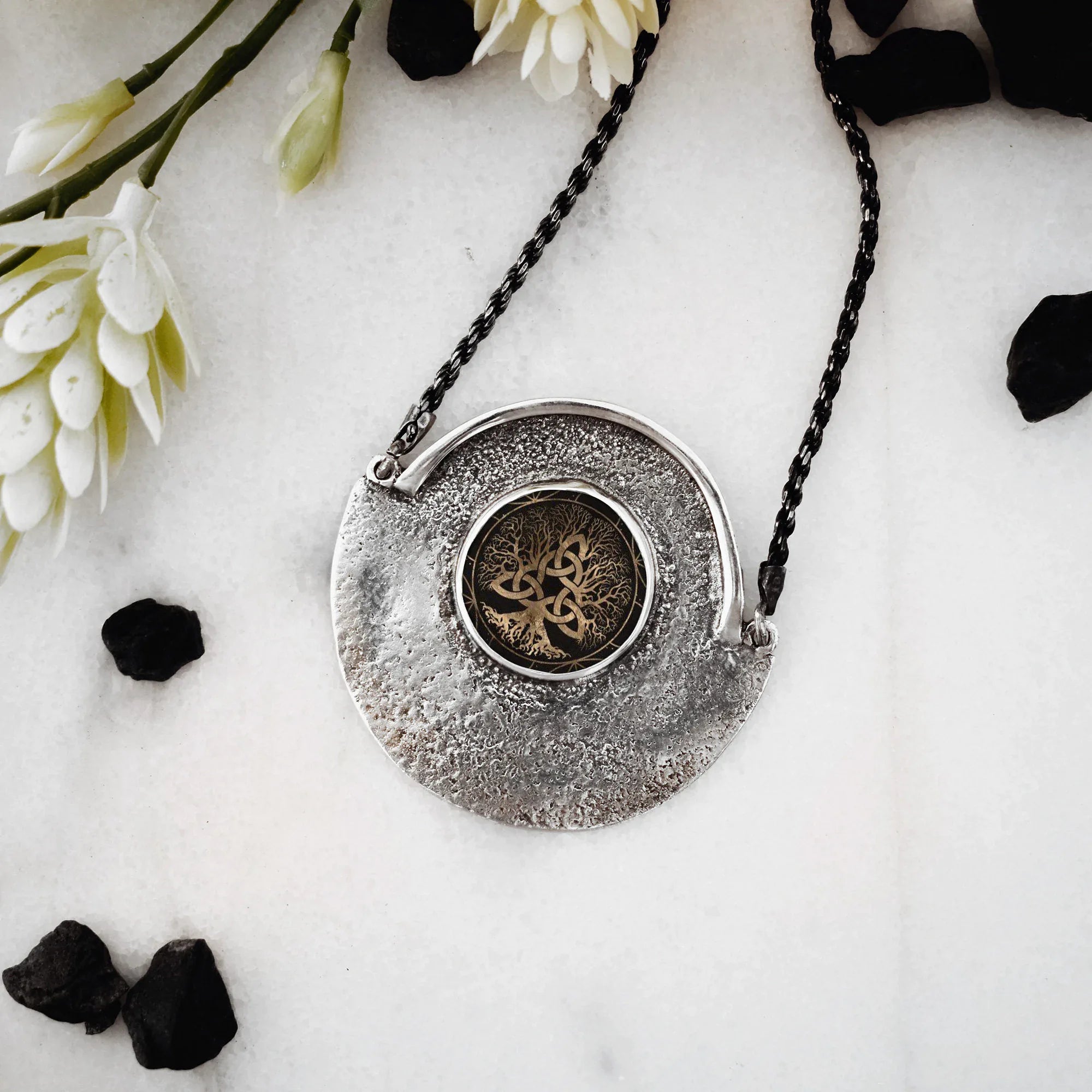 Silver pendant necklace with intricate design on a white surface with flowers and black stones.