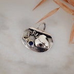 Close-up of a small oval oxidised silver pendant showing the raised polished heart, deep blue lapis lazuli stone, wire scroll and silver granule detail against the dark oxidised background.