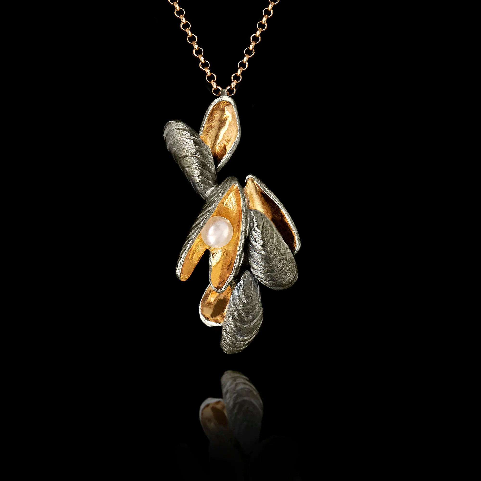 Handcrafted 925 sterling silver shell cluster pendant with dark oxidised exterior and gold-plated interior shell forms cradling a freshwater pearl, hanging on a gold chain against a black background. Main image