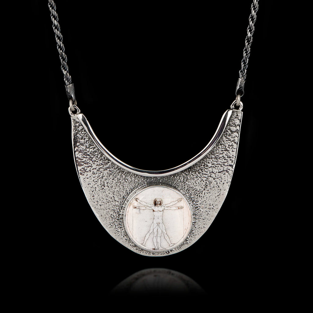 Unique 925 sterling silver statement necklace featuring a round ceramic Vitruvian Man by Da Vinci, set in a textured hammered silver crescent frame.