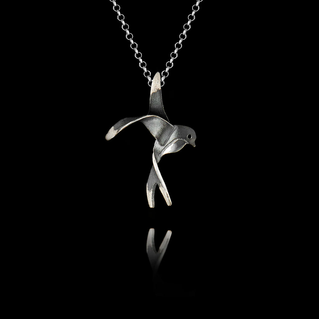 Handcrafted 925 sterling silver swallow pendant with oxidised finish showing the bird with outstretched wings and forked tail in a mid-flight pose, hanging on a silver chain against a black background.