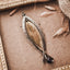 Long fish pendant with a sand-textured oxidised silver outer frame, gold-plated inner body and forked tail with an amethyst bead drop, displayed on a brown surface with a vintage gold frame and dried grasses.