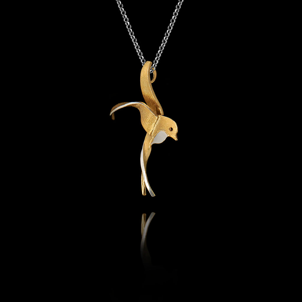 Side angle view of a sterling silver gold-plated swallow pendant with rhodium accent showing the fluid sculpted silhouette of a swallow in flight on a silver chain against a black background.
