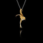 Side angle view of a sterling silver gold-plated swallow pendant with rhodium accent showing the fluid sculpted silhouette of a swallow in flight on a silver chain against a black background.
